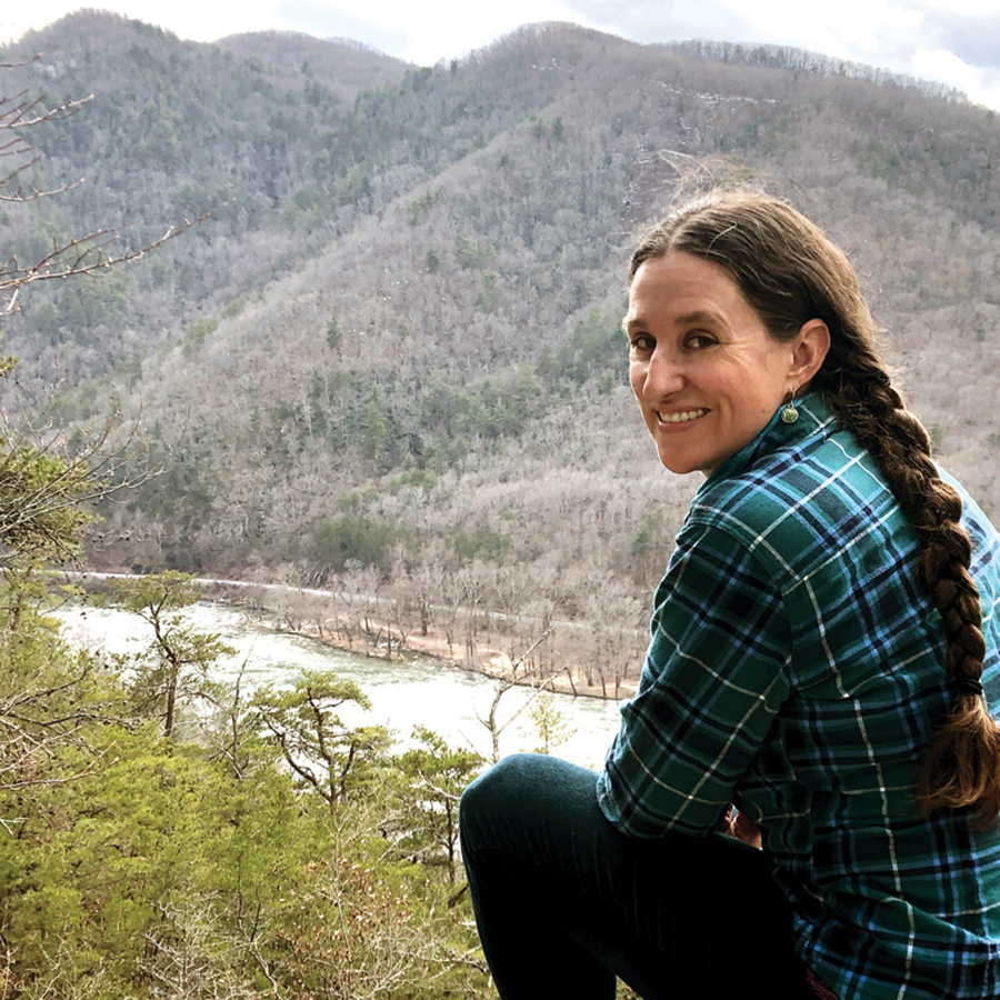 Sarah Jones Decker sitting on a rock in front of a mountain and river