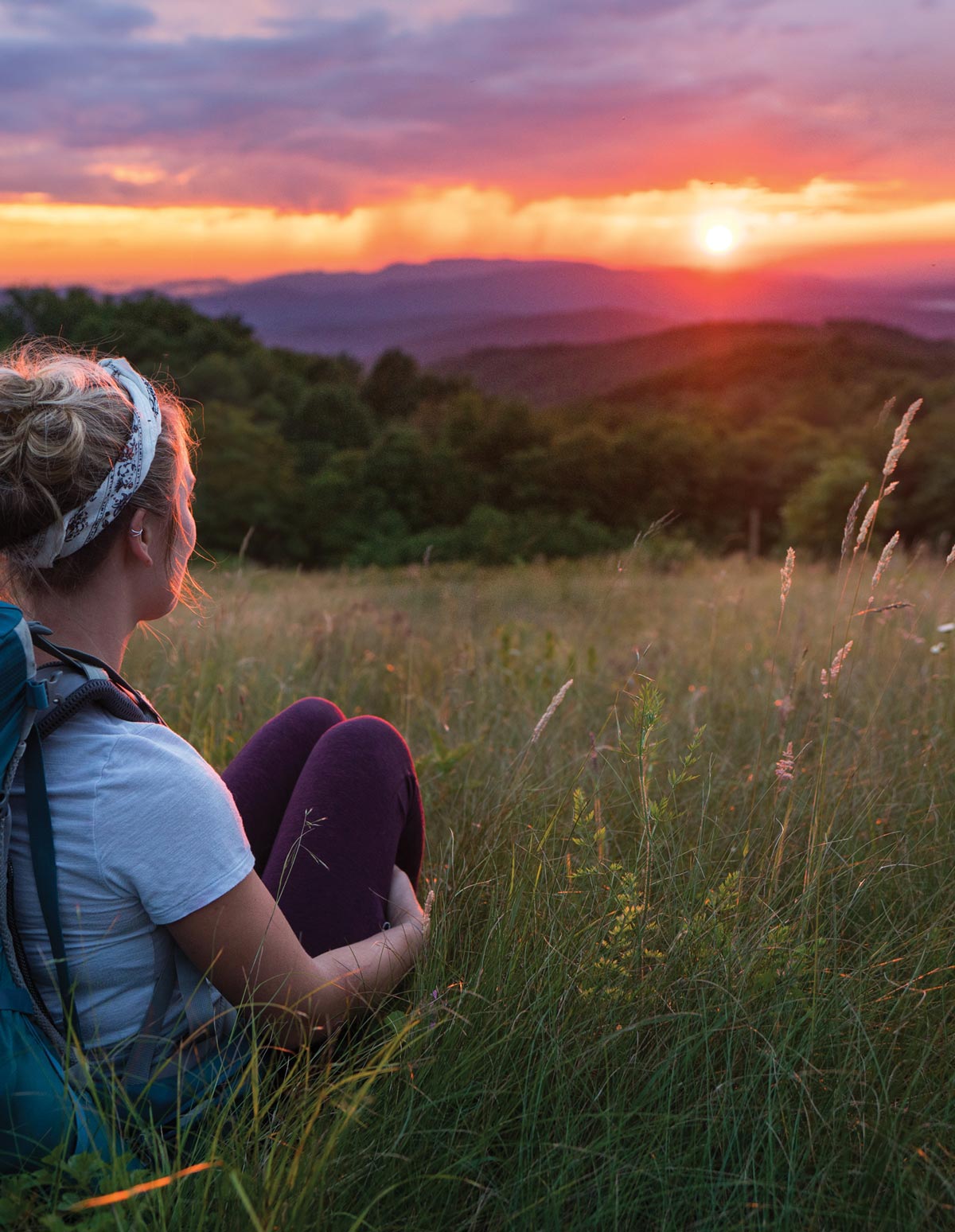 girl in hiking gear sitting in a meadow watching the sunset