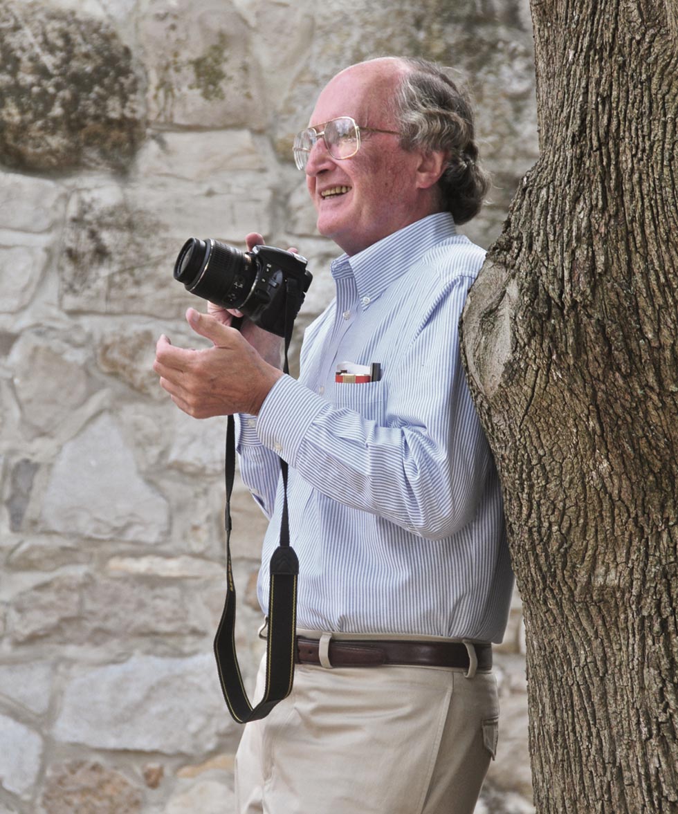 Brian King holding a camera and leaning against a tree