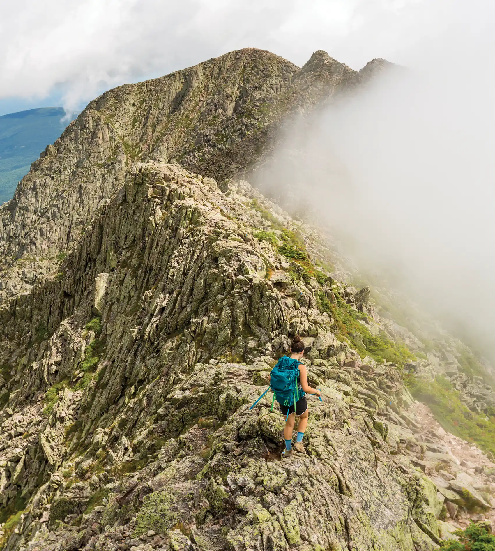 Hiker on large mountain top with clouds in distance