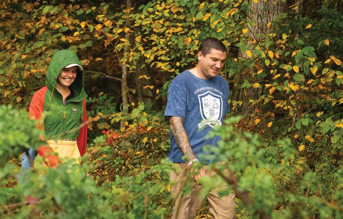 a man and a women smile among a sea of leaves while out on a hike