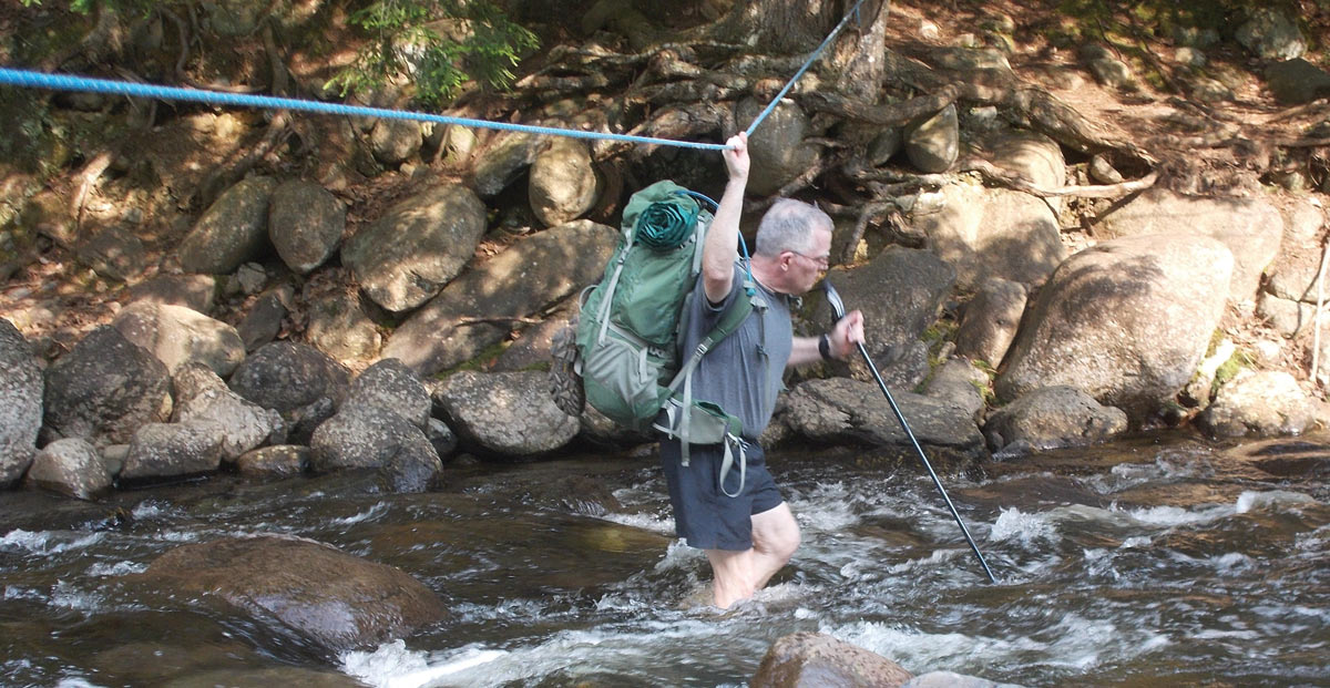 Don DeArmon using a rope to cross a stream