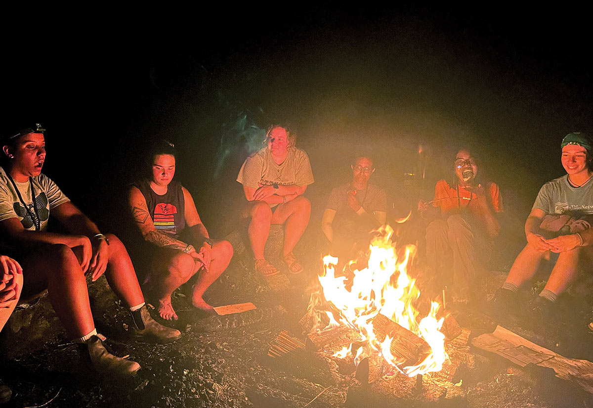 a group of young adult sit around camp fire at night