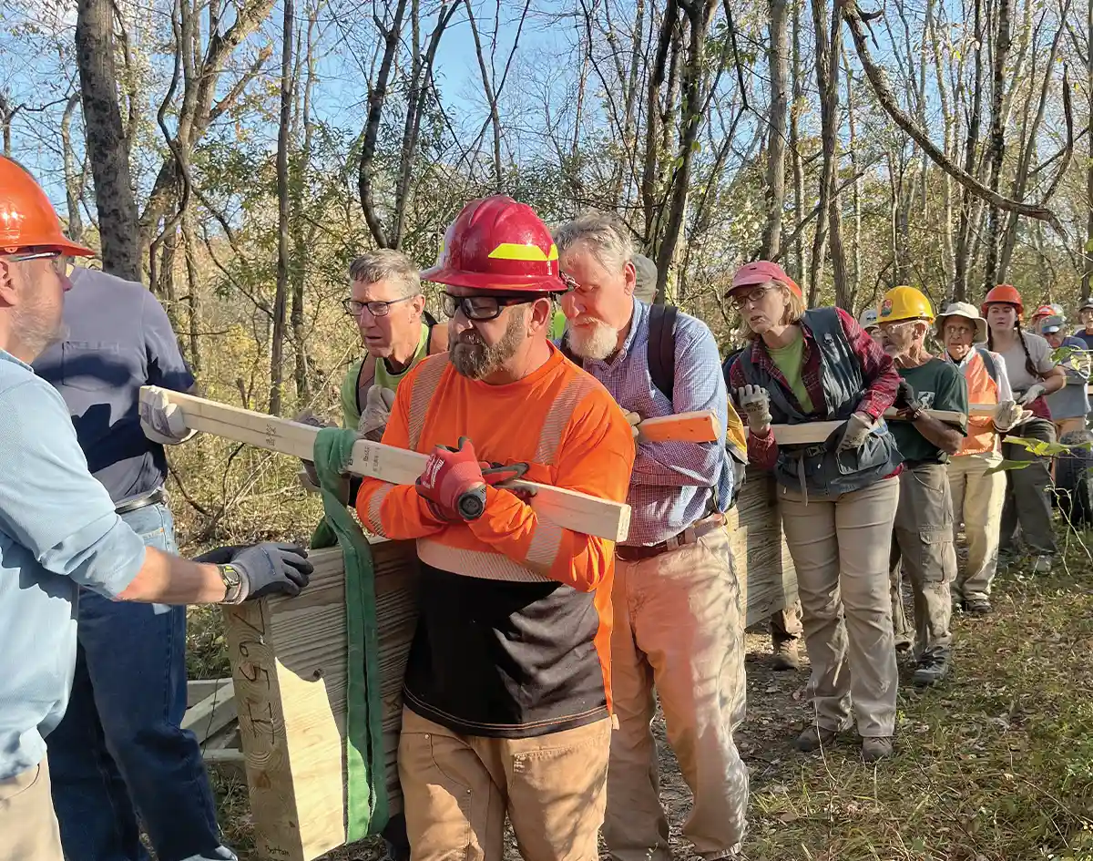 Volunteers in hard hats carrying lumber on a trail work project.