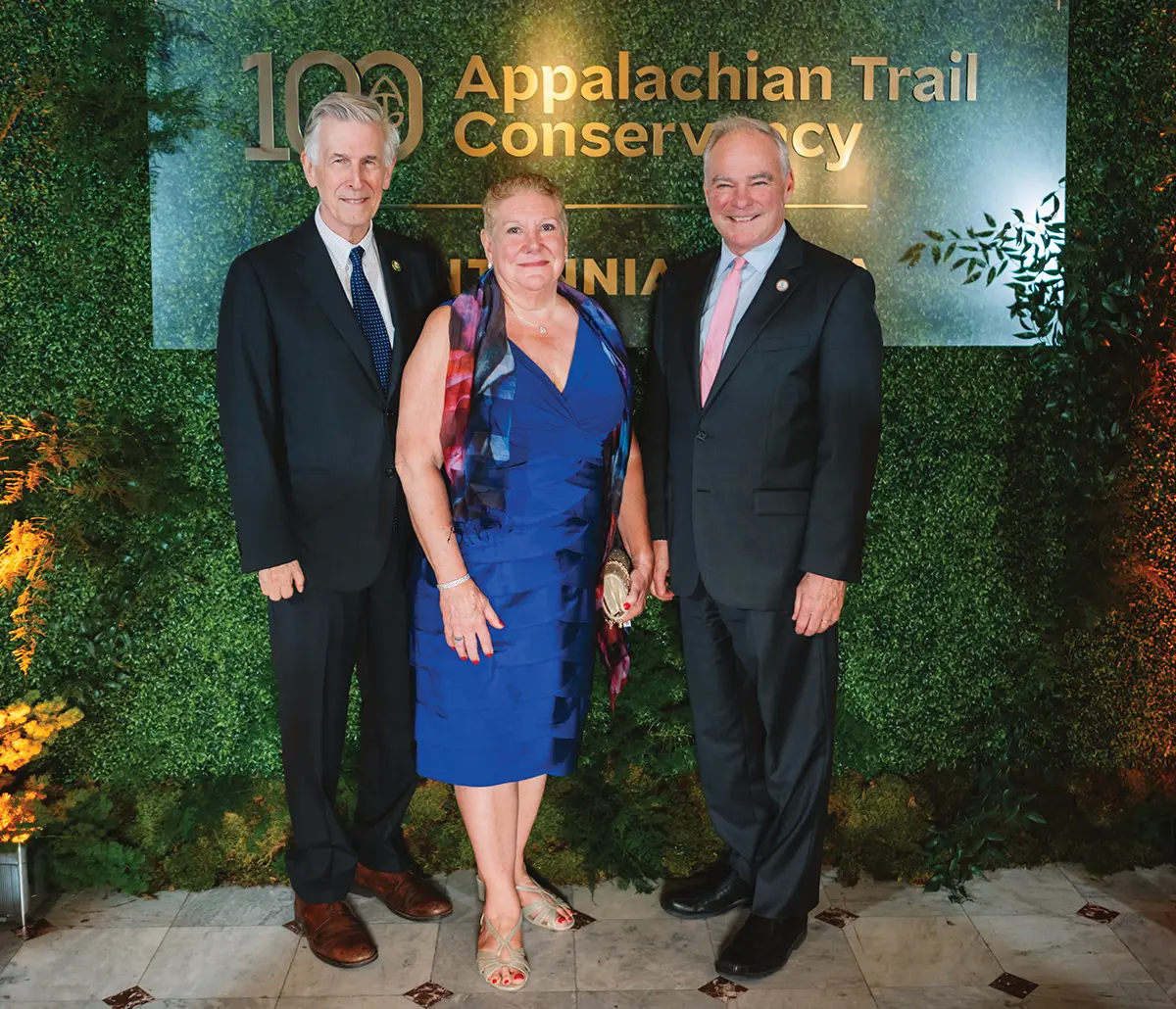 Three people posing in front of an Appalachian Trail Conservancy banner.