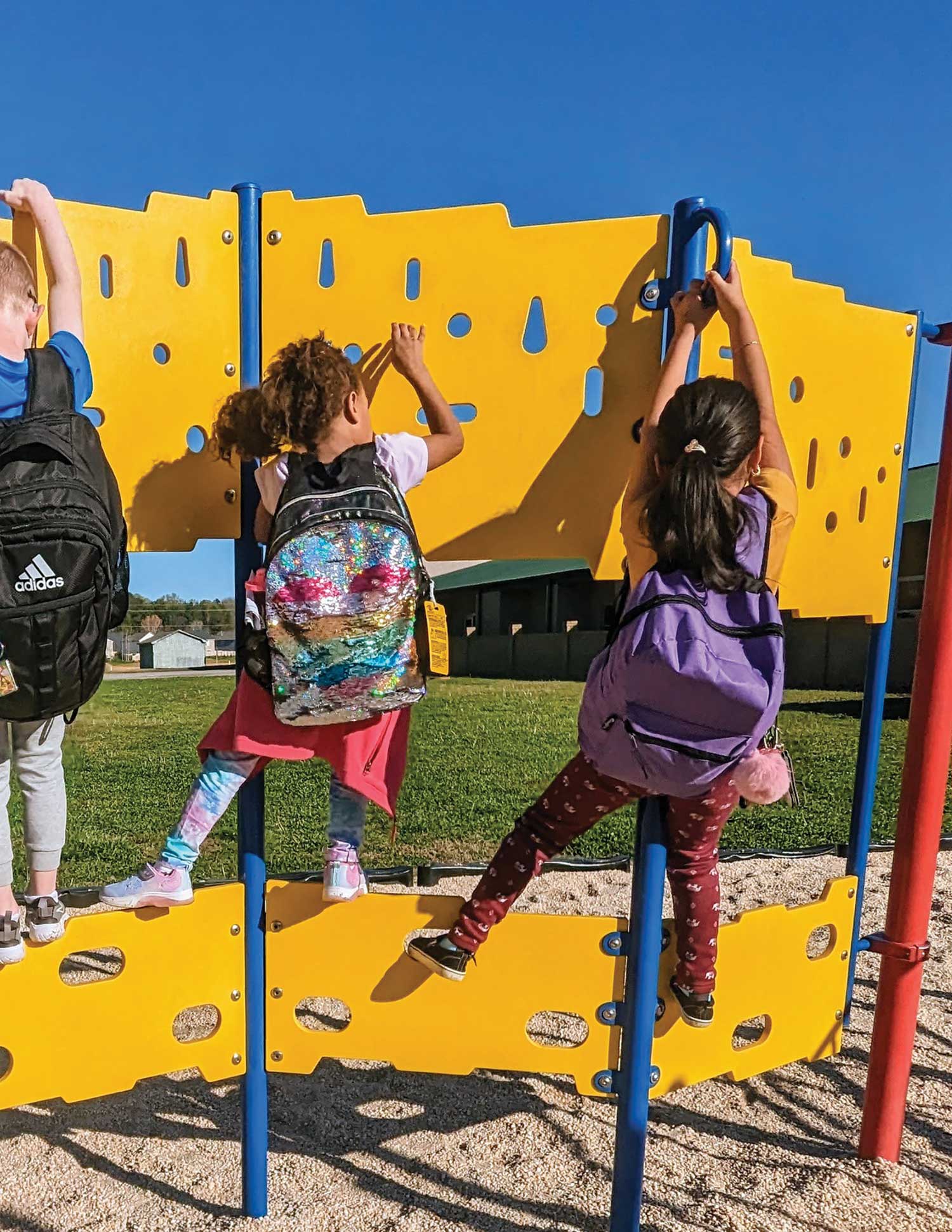 students wearing backpacks while using the school’s yellow, blue, and red colored playground