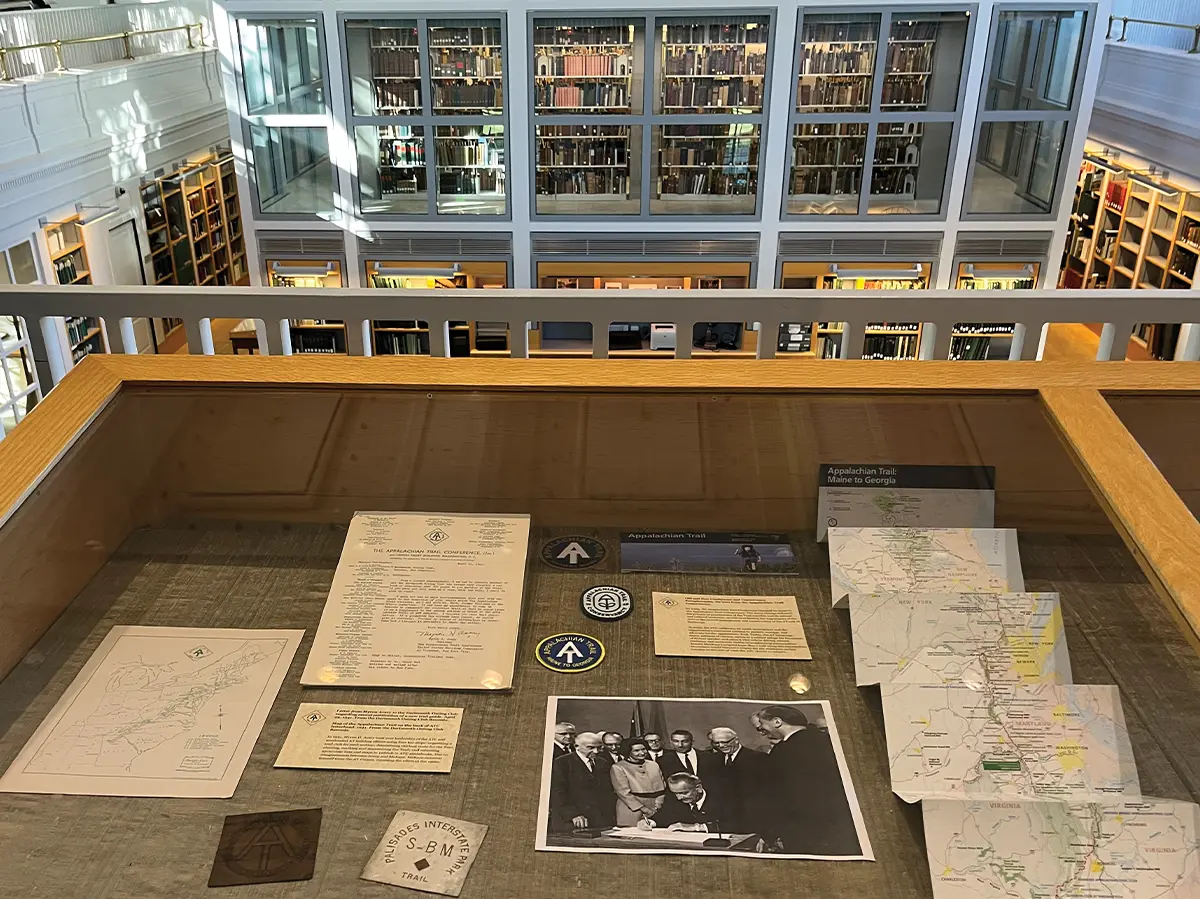 Museum exhibit display case containing historic Appalachian Trail documents, maps, trail markers, and a black and white photo of the trail's founders.
