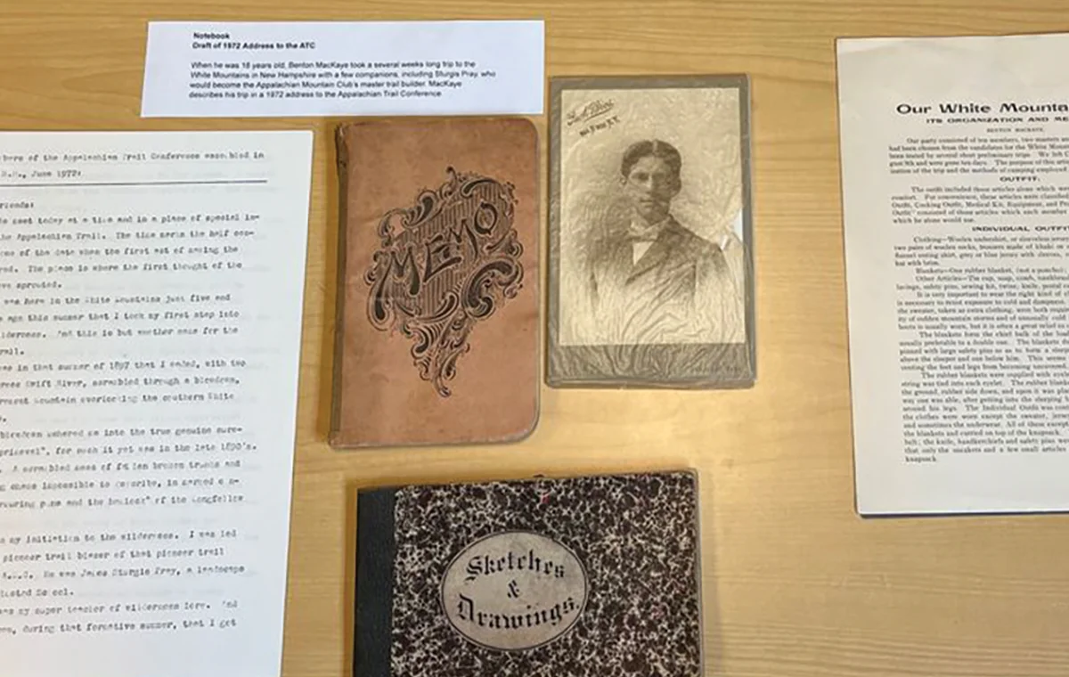 Close-up of Appalachian Trail historical documents: A memo book, a photo of Benton MacKaye, an old sketches book, and a brochure about trail outfitting.