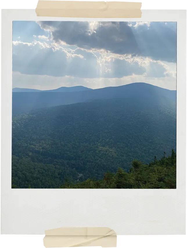 A scenic view of layered mountain ridges under dramatic clouds with beams of sunlight shining through onto the landscape.