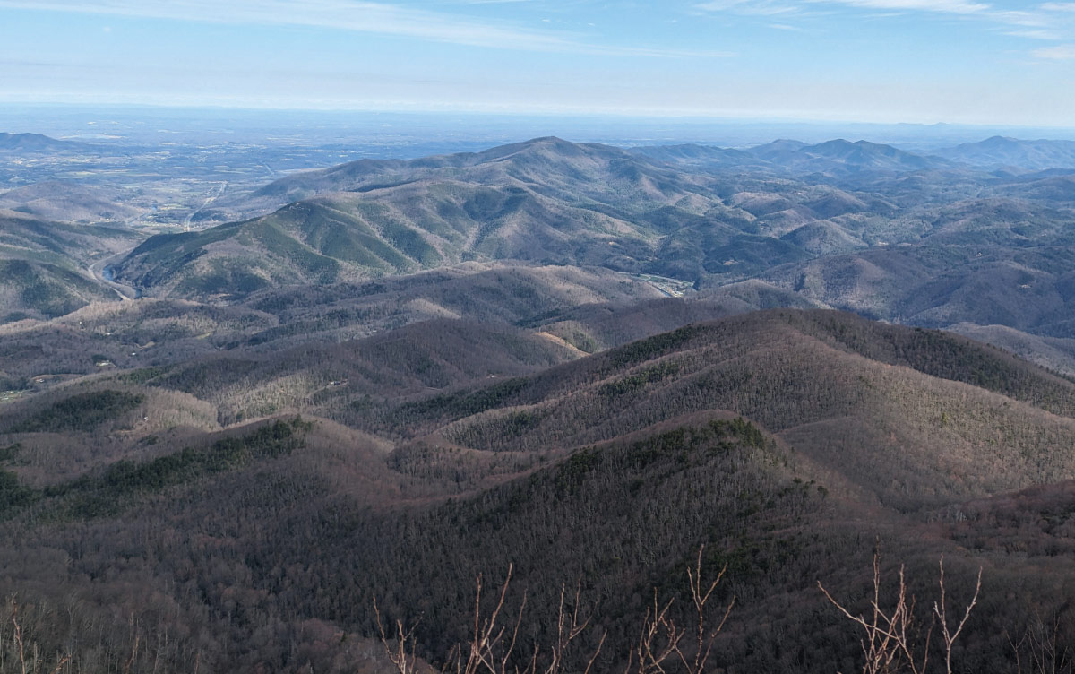 A wide panoramic view from a high elevation looking out over endless rolling blue and purple mountain ridges under a clear sky.