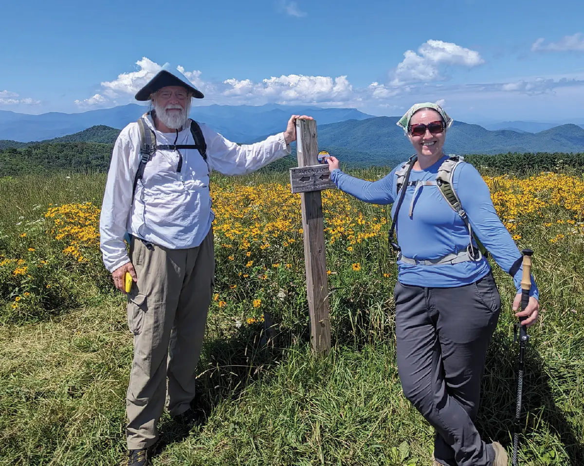 Monica Mogilewsky with Morgan Sommerville (ATC’s Director of VUM) smiling at Max Patch, NC; Both are leaning against a wooden trail marker post