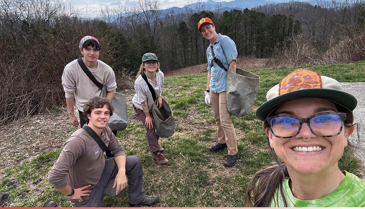 A smiling group of young outdoor workers poses for a selfie on a mountain hillside.