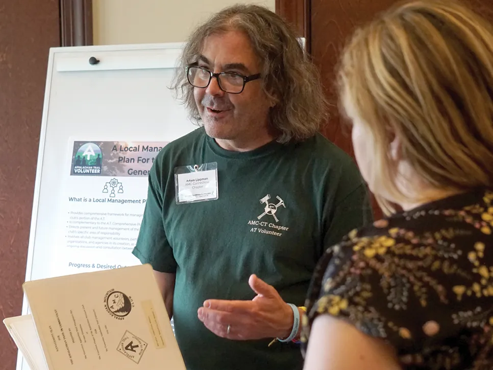 Appalachian Trail volunteer speaks with an attendee while holding a binder at a local trail management workshop.